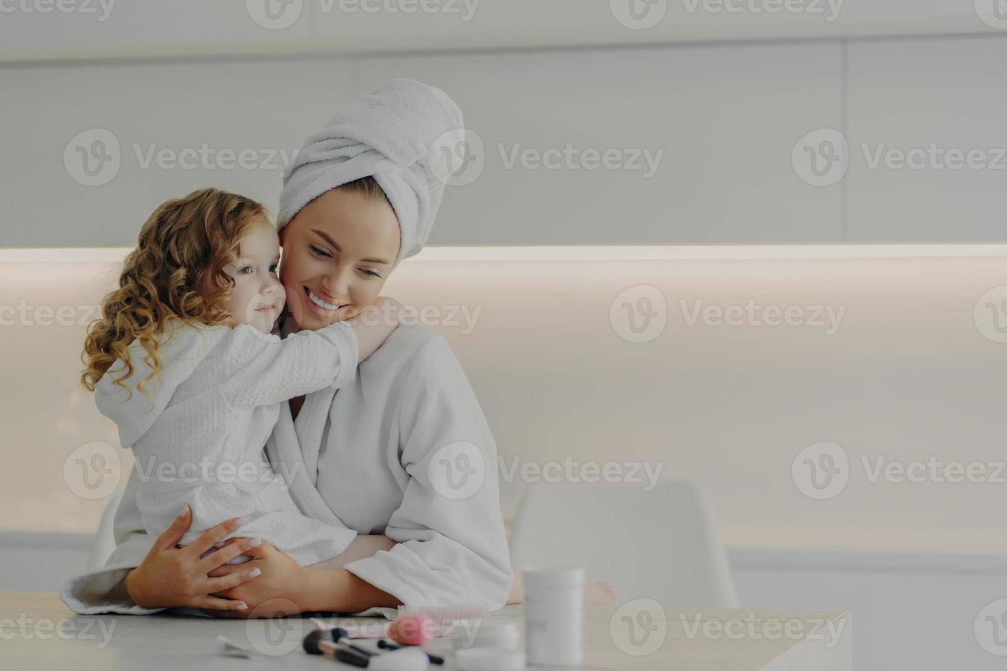 Mutter und süße kleine Tochter in weißen Bademänteln umarmen und genießen das Wochenende zusammen zu Hause foto