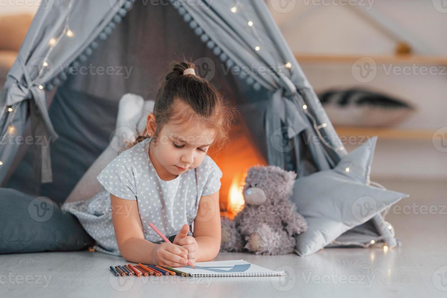 Brief schreiben. süßes kleines Mädchen, das im Zelt spielt, das sich im Wohnraum befindet foto