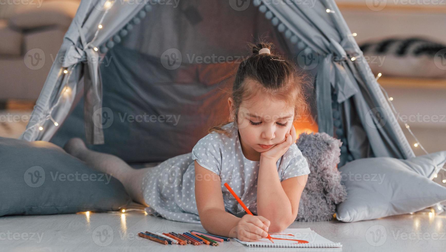 Konzeption von Bildung. süßes kleines Mädchen, das im Zelt spielt, das sich im Wohnraum befindet foto