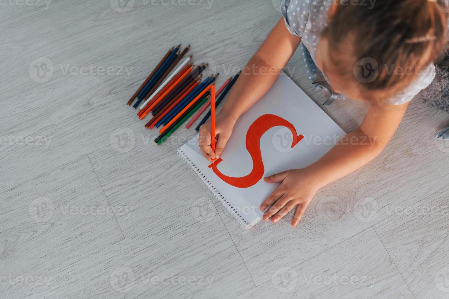 Draufsicht des kleinen Mädchens, das einen Brief schreibt, wenn es sich zu Hause auf den Boden legt foto