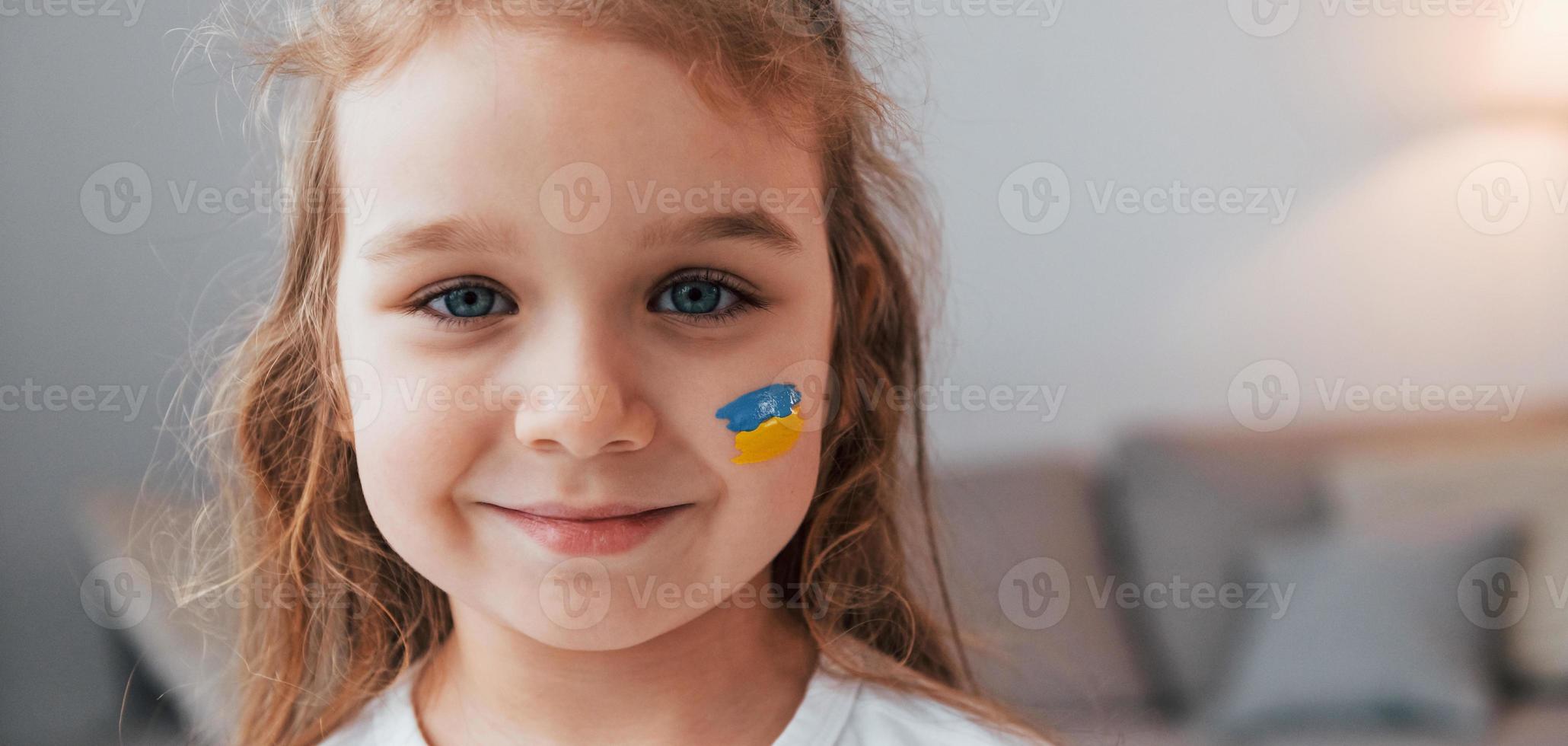 lächeln und gute Laune haben. Porträt eines kleinen Mädchens mit ukrainischer Flagge im Gesicht foto