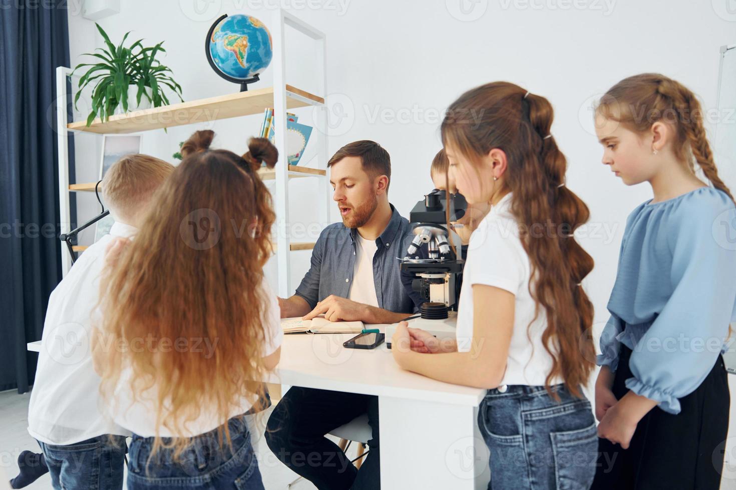 Konzeption des Biologieunterrichts. Mikroskop verwenden. gruppe von kinderschülern im unterricht in der schule mit lehrer foto