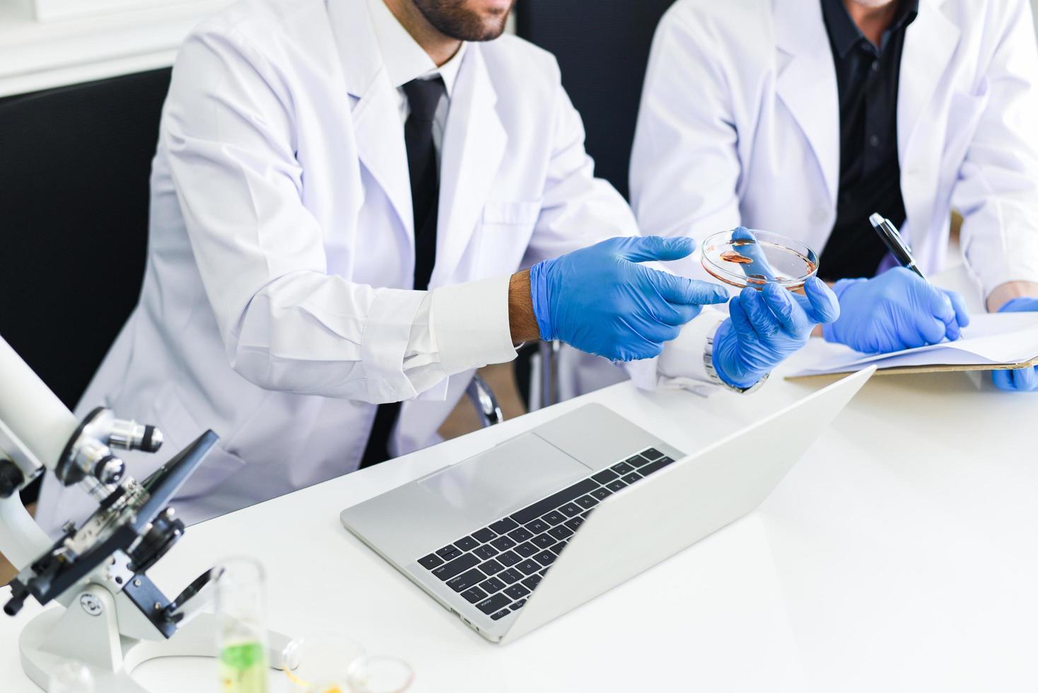 ein team von wissenschaftlern arbeitet im labor - männliche arztforscher führen untersuchungen mit mikroskop und laptop im konzept der bluttestergebnisse der biochemie der genetik der forensik durch foto