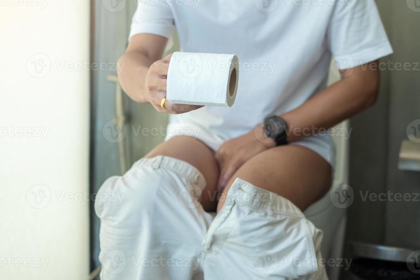 mann, der toilettenpapierrolle hält, während er auf der toilettenschüssel sitzt. Durchfall, Verstopfung, Infektion, Bauchschmerzen, Magenschmerzen, Zystitis, Versicherung und medizinisches Konzept foto