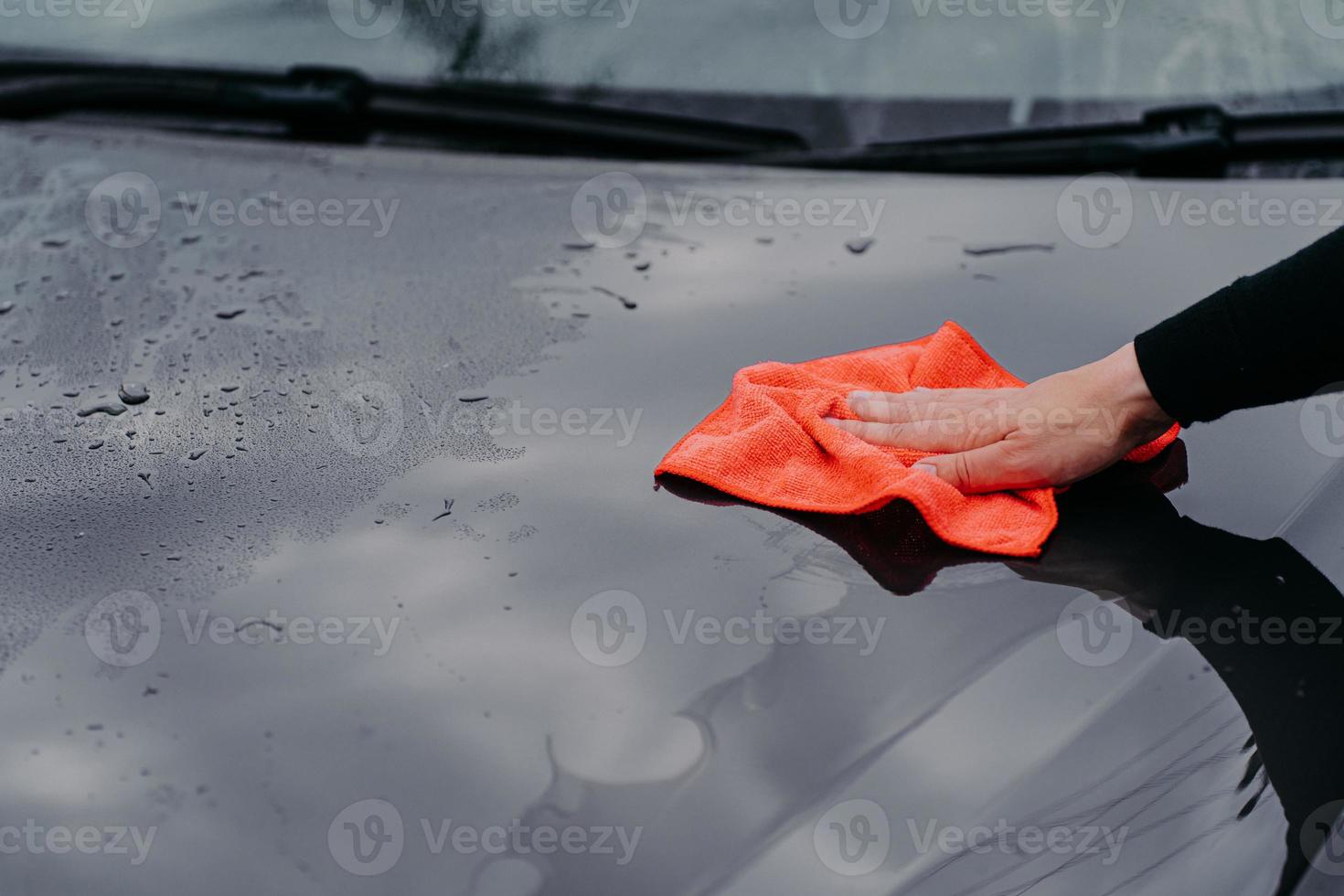 Auto mit Mikrofasertuch reinigen. Mann wäscht schwarze Motorhaube. Fahrzeug polieren. Fahrzeugaufbereitung, Wartung foto