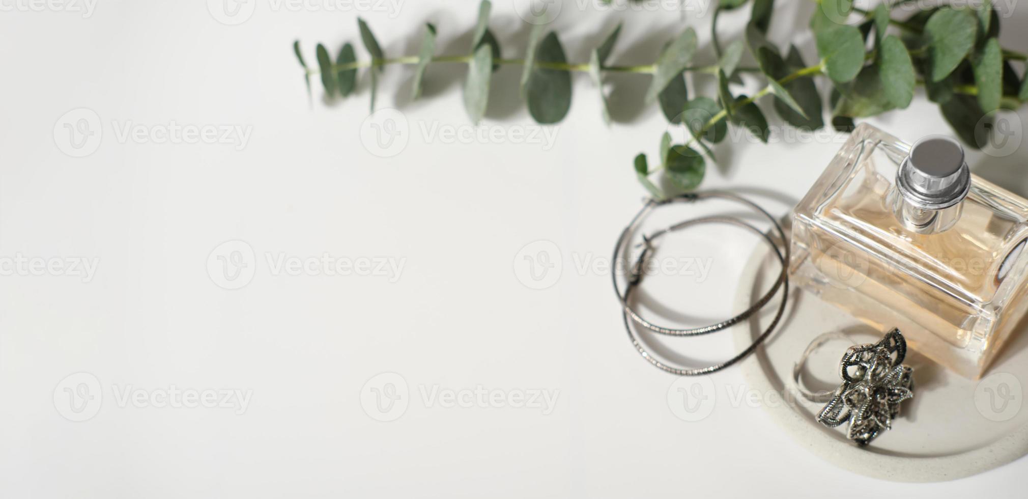 Flasche Parfüm und weiblicher Schmuck auf grauer Betonplatte und Eukalyptuszweig auf weißem Tisch. Banner. Accessoires für die Frau. luxuriöser Lebensstil. foto