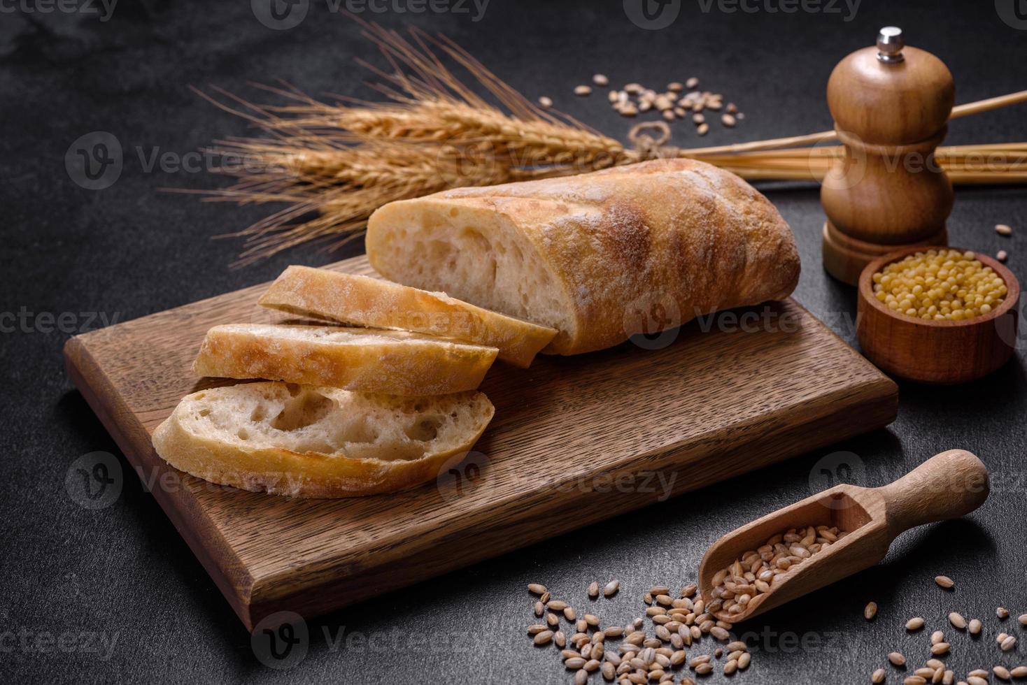 Französisches Baguette-Brot, geschnitten auf einem Holzschneidebrett vor dunklem Betonhintergrund foto