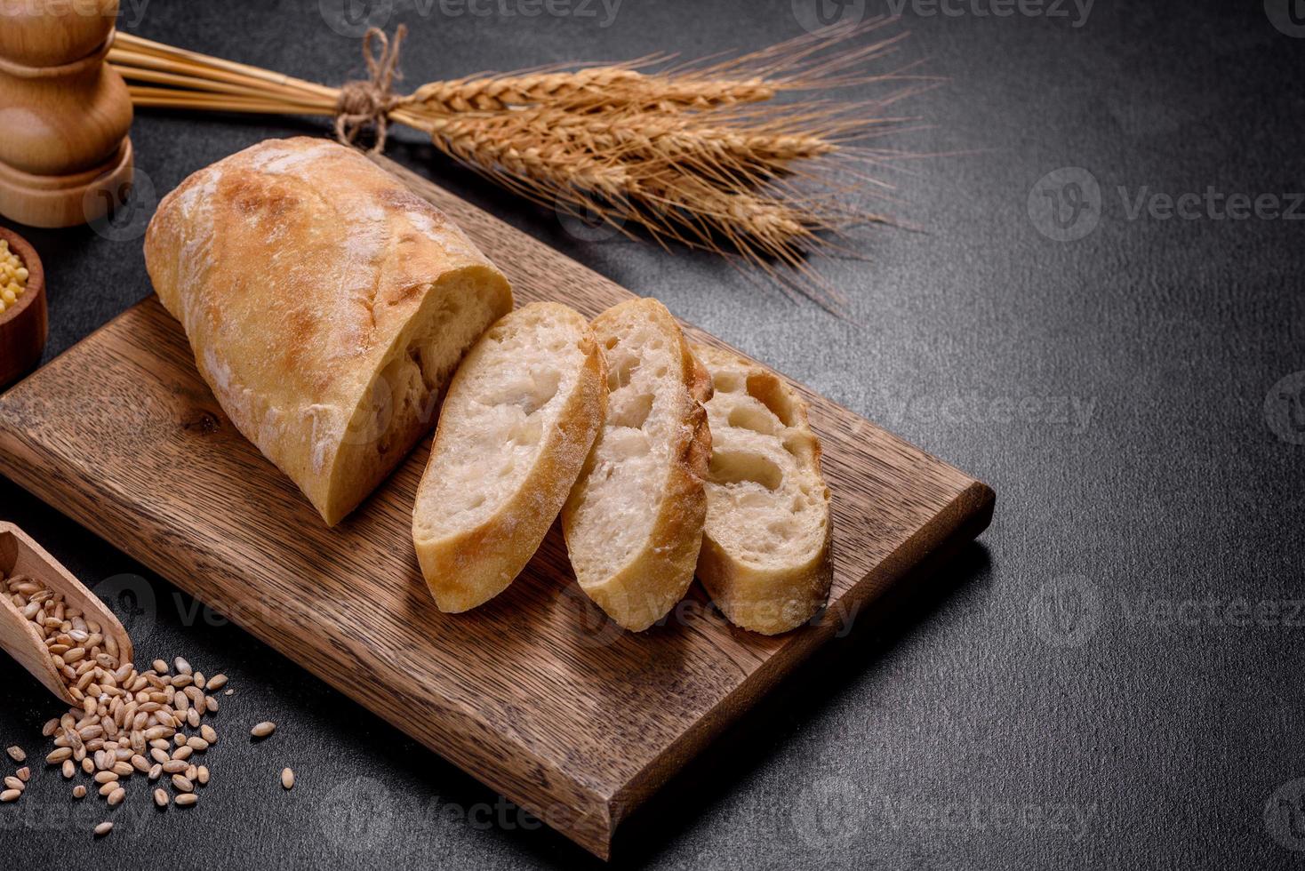 Französisches Baguette-Brot, geschnitten auf einem Holzschneidebrett vor dunklem Betonhintergrund foto