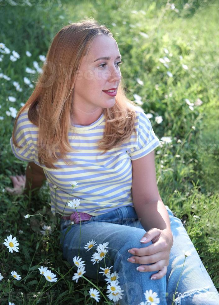 schöne Frau, die auf einer Wiese sitzt und beiseite schaut. foto