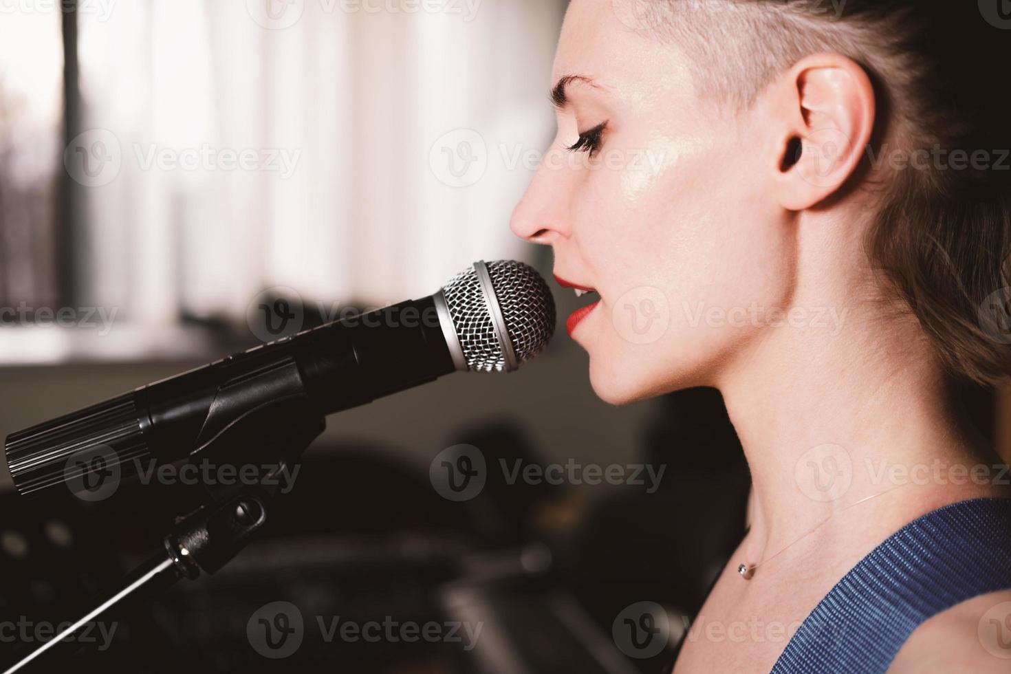 junge rocksängerin mit mikrofon, singen. Seitenansicht. Nahansicht. Frau mit kurzen Haaren auf einer Bühne. Live-Musik-Performance foto