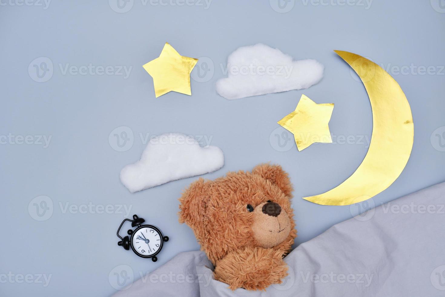 Teddybär schläft unter Decke auf grauem Hintergrund foto
