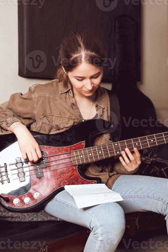 junge Frau, die Bassgitarre spielt und Akkordnoten betrachtet. Übungsraum. weibliche Rockmusikerin. vertikale Größe foto