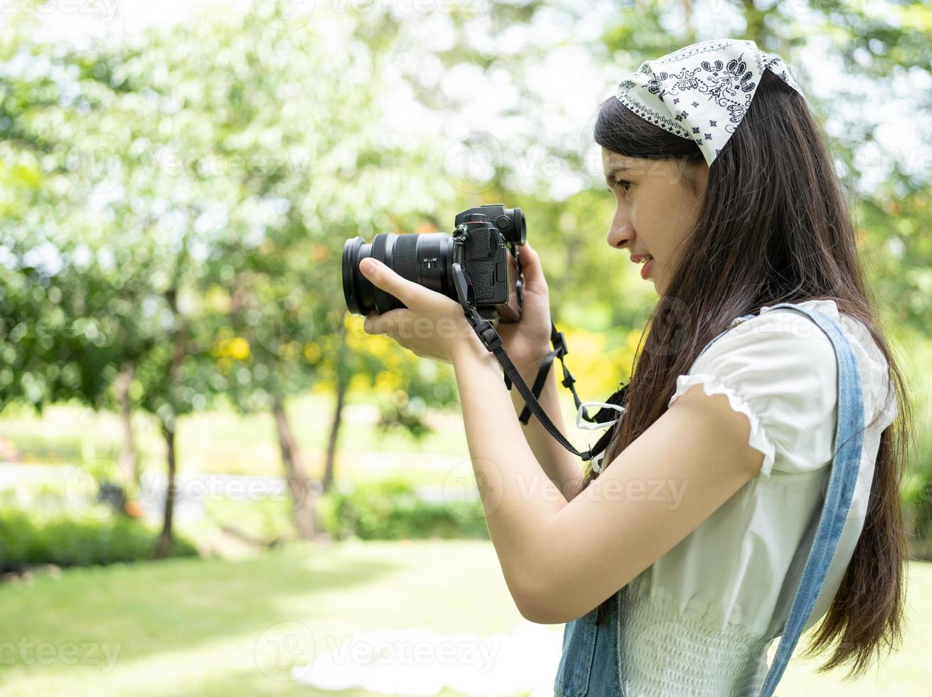 schöne Frau hält Digitalkamera und macht verschwommenen Hintergrund. Hinter den Kulissen steht ein junger asiatischer Fotograf im grünen Park und fotografiert als Erholung. Konzept zum Fotografieren von Touristen. foto