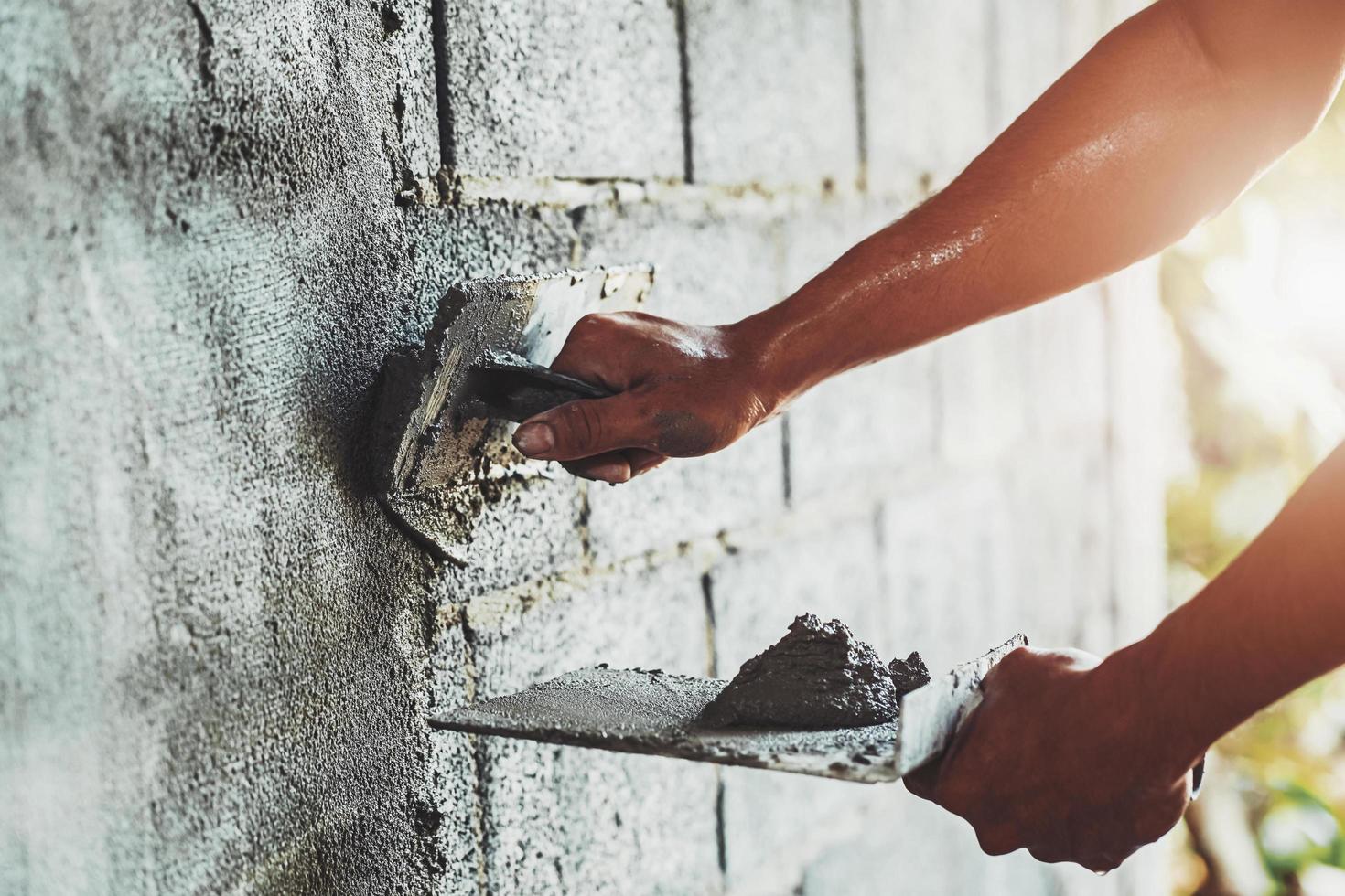 Nahaufnahmehand des Arbeiters, der Zement an der Wand für den Hausbau verputzt foto