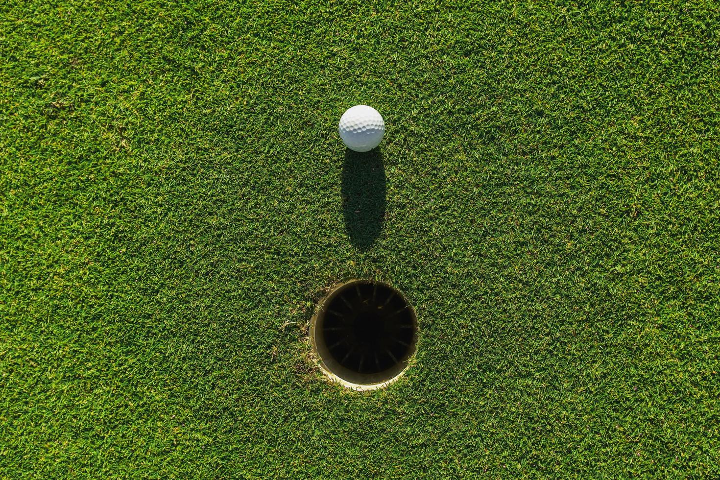 Golfball auf grünem Gras mit Loch und Sonnenlicht foto