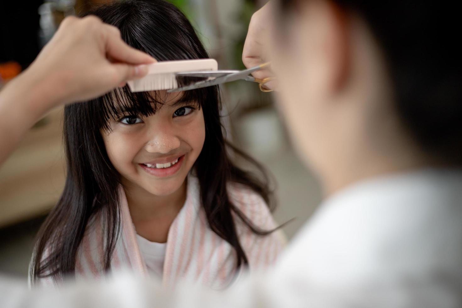 asiatische mutter schneidet ihrer tochter im wohnzimmer zu hause die haare, während sie während der sperrung zu hause sicher vor dem covid-19-coronavirus bleibt. selbstquarantäne und soziales distanzierungskonzept. foto