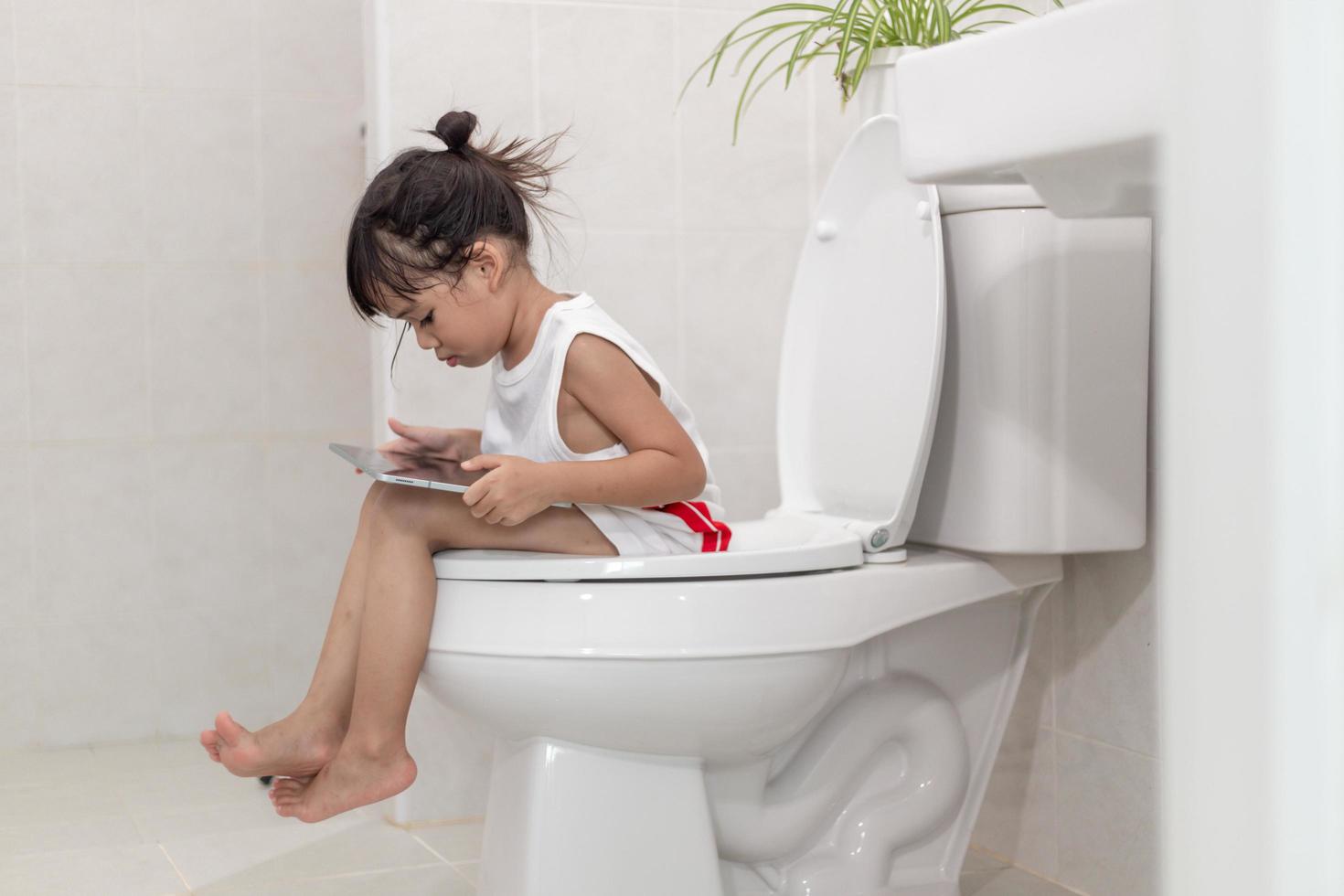 kind, das auf der toilette sitzt und das tablet hält. kindersüchtiges smartphone-konzept foto