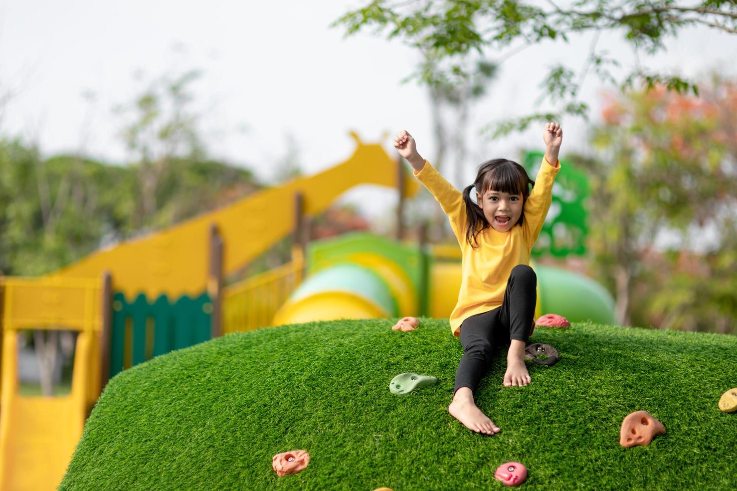 süßes asiatisches mädchen, das spaß hat, auf künstlichen felsbrocken auf dem schulhofspielplatz zu klettern, kleines mädchen, das die felswand hochklettert, hand-auge-koordination, fähigkeitsentwicklung foto