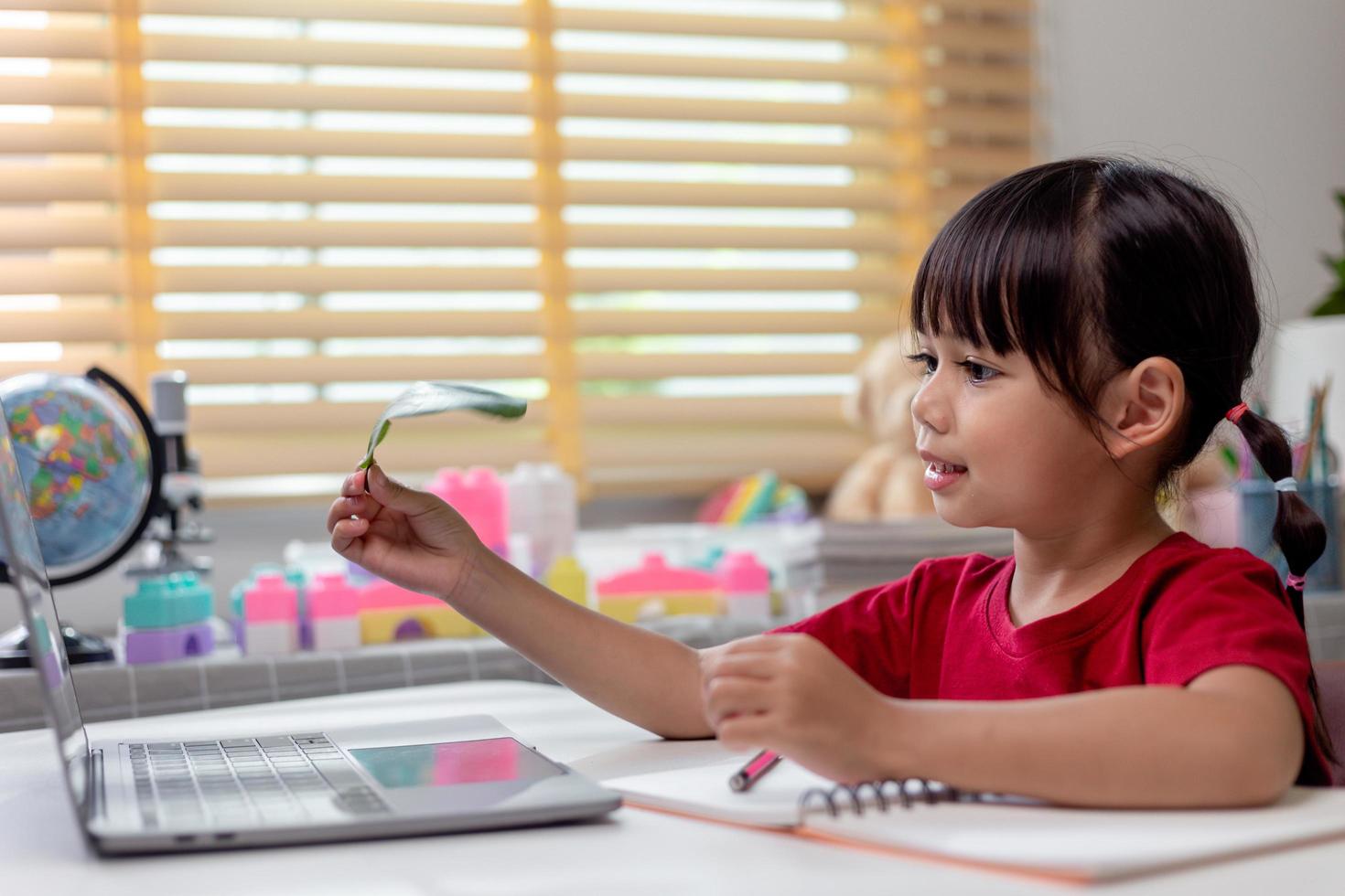 Lernzeit. interessiertes kleines Schulmädchen im Headset sitzt zu Hause am Schreibtisch und sieht sich die Videostunde zur Bildung an. neugieriges kleines Mädchen im schulpflichtigen Alter denkt an die Frage des Lehrers und wählt die richtige Antwort auf dem Laptop-Bildschirm aus foto