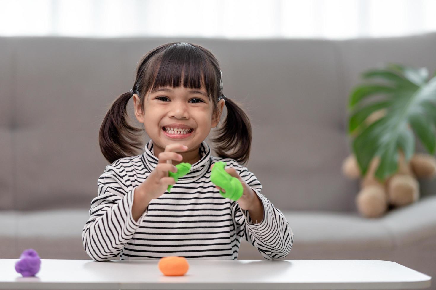 Das kleine Mädchen lernt, in einem gut beleuchteten Raum mit buntem Knete zu spielen foto