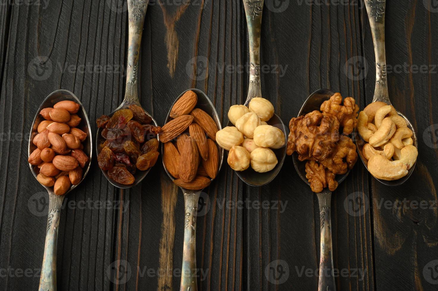 Haselnüsse, Cashewnüsse, Rosinen, Mandeln, Erdnüsse, Walnüsse in silbernen Löffeln auf rustikalem Hintergrund foto