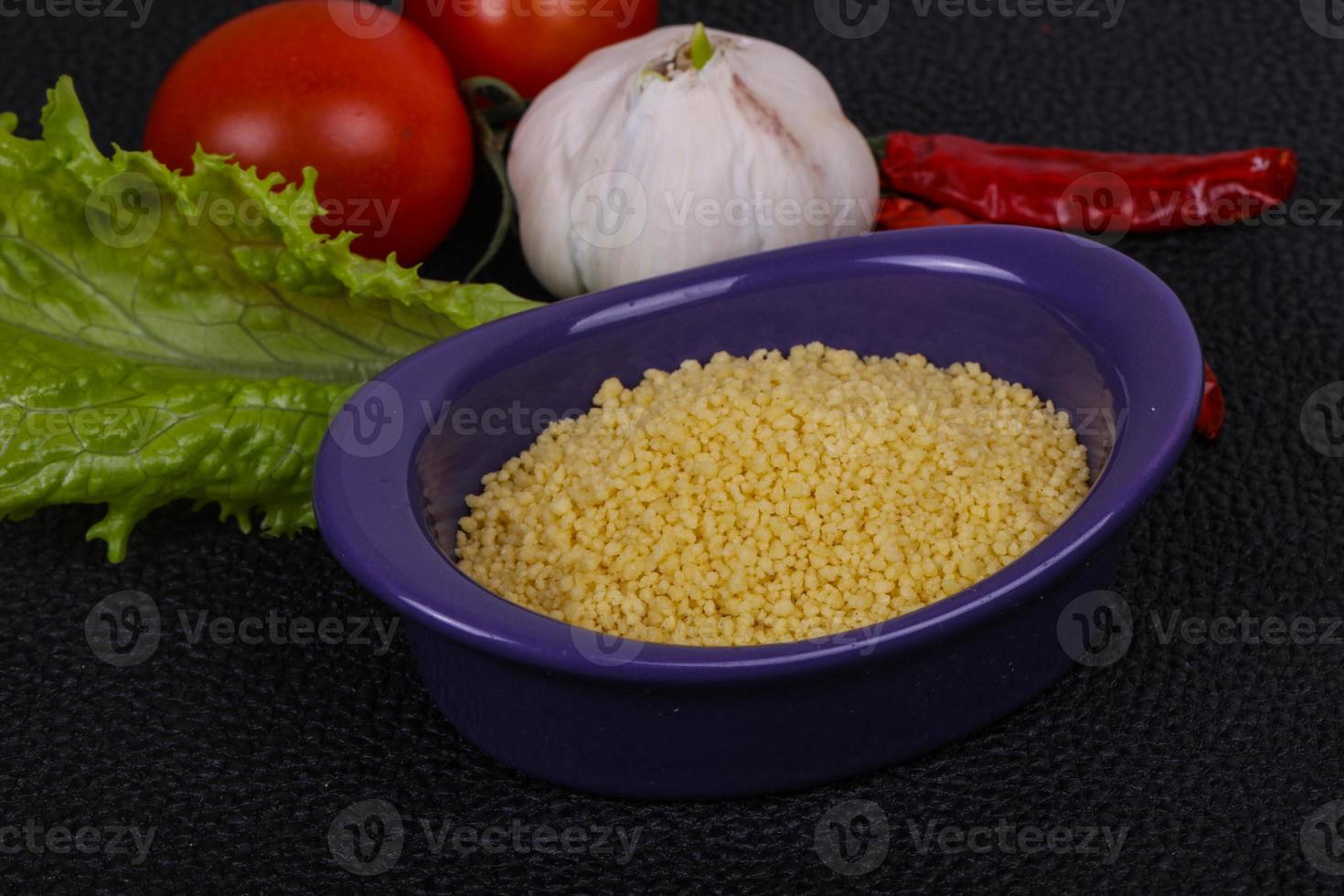 roher Couscous in der Schüssel serviert Salatblätter, Tomaten und Paprika foto