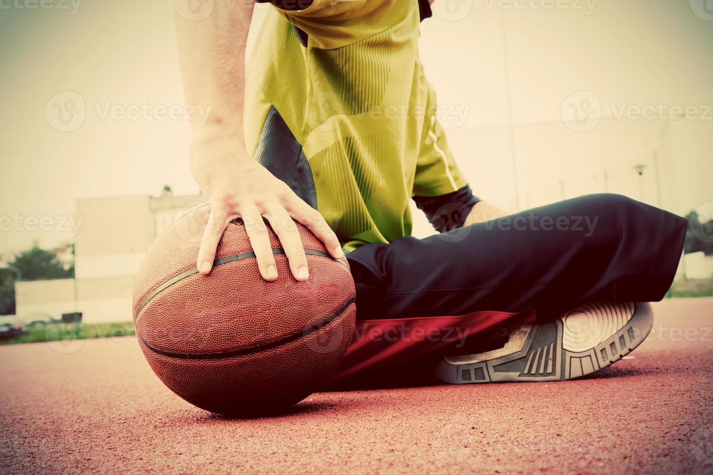 junger Mann auf dem Basketballplatz. Sitzen und Dribbeln mit Ball foto