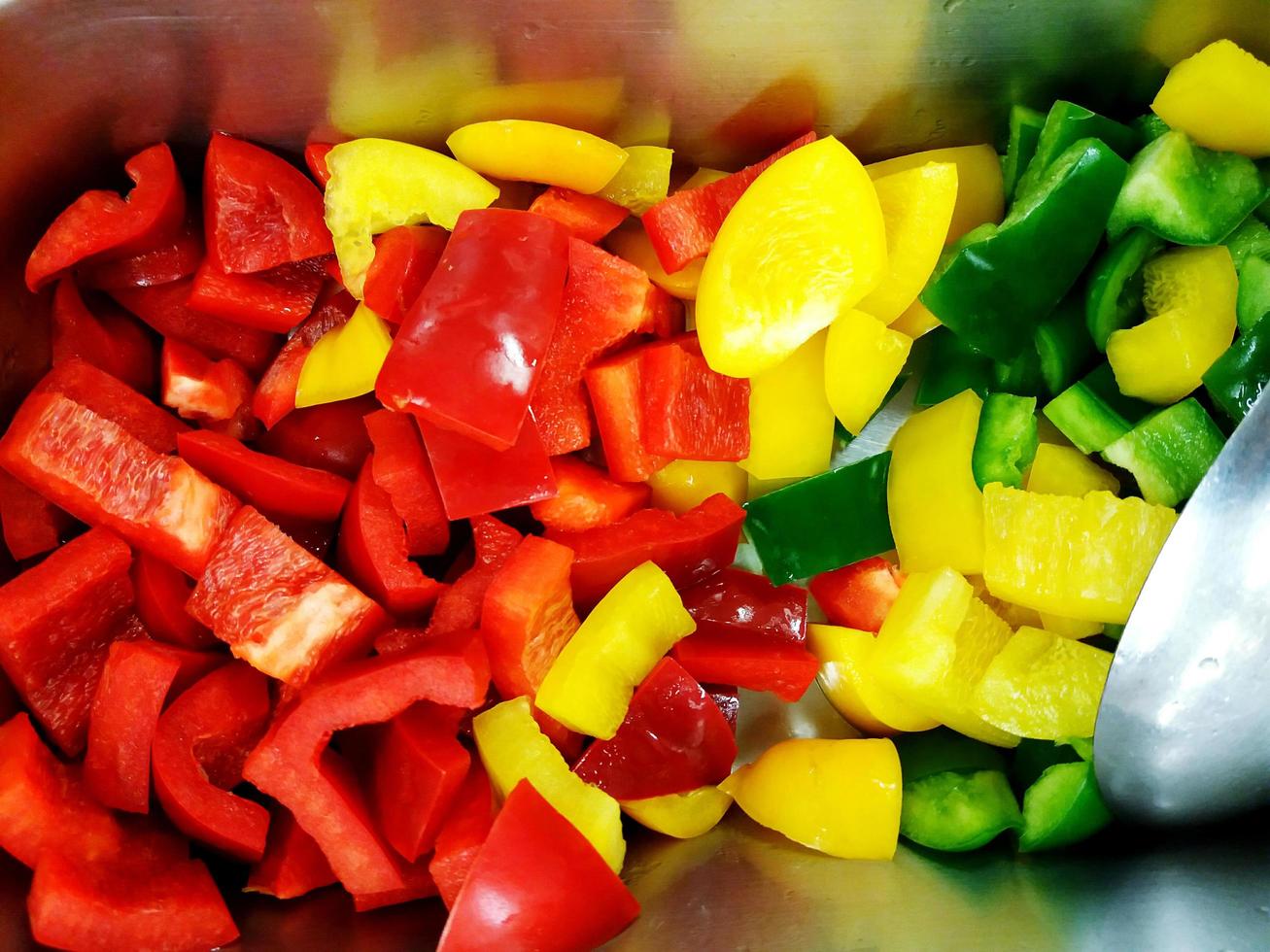 Viele Scheiben roter, gelber und grüner Paprika oder süßer Chili mit Metalllöffel auf dem Stahlblech auf der Salatbar foto