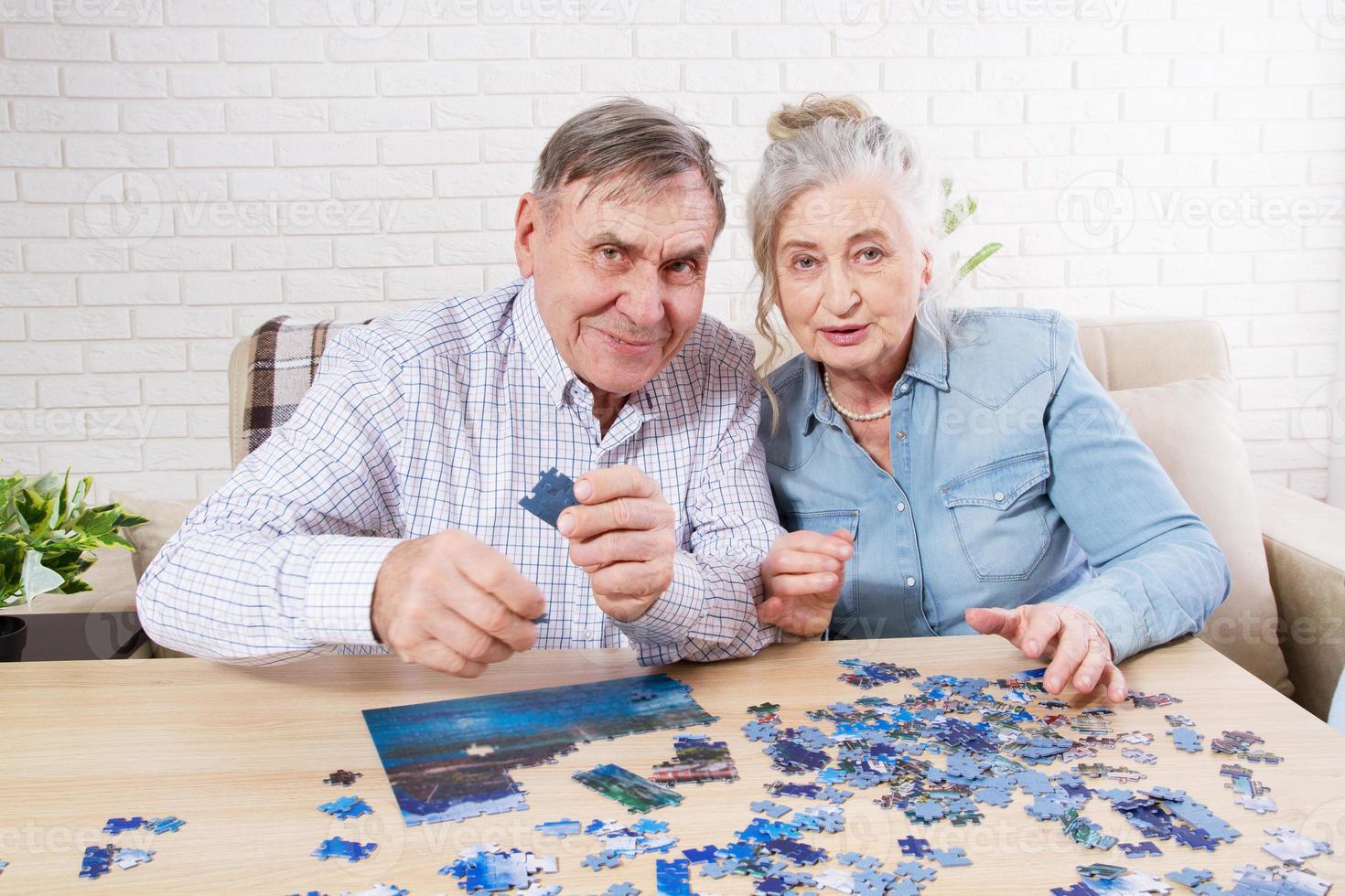 süßes älteres paar, das zu hause zusammen puzzle löst. foto