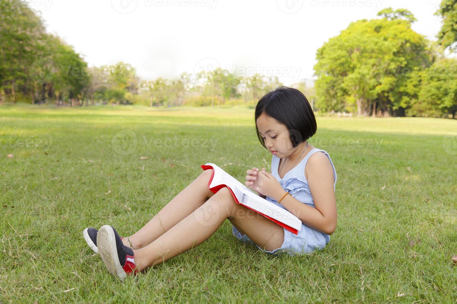 Asiatisches kleines Mädchen liest Buch im Park foto