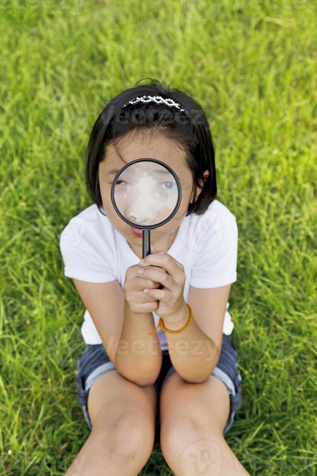 Asiatisches kleines Mädchen, das eine Lupe im Freien hält foto