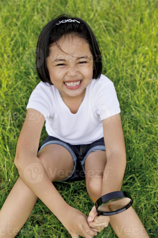 Asiatisches kleines Mädchen, das eine Lupe im Freien hält foto