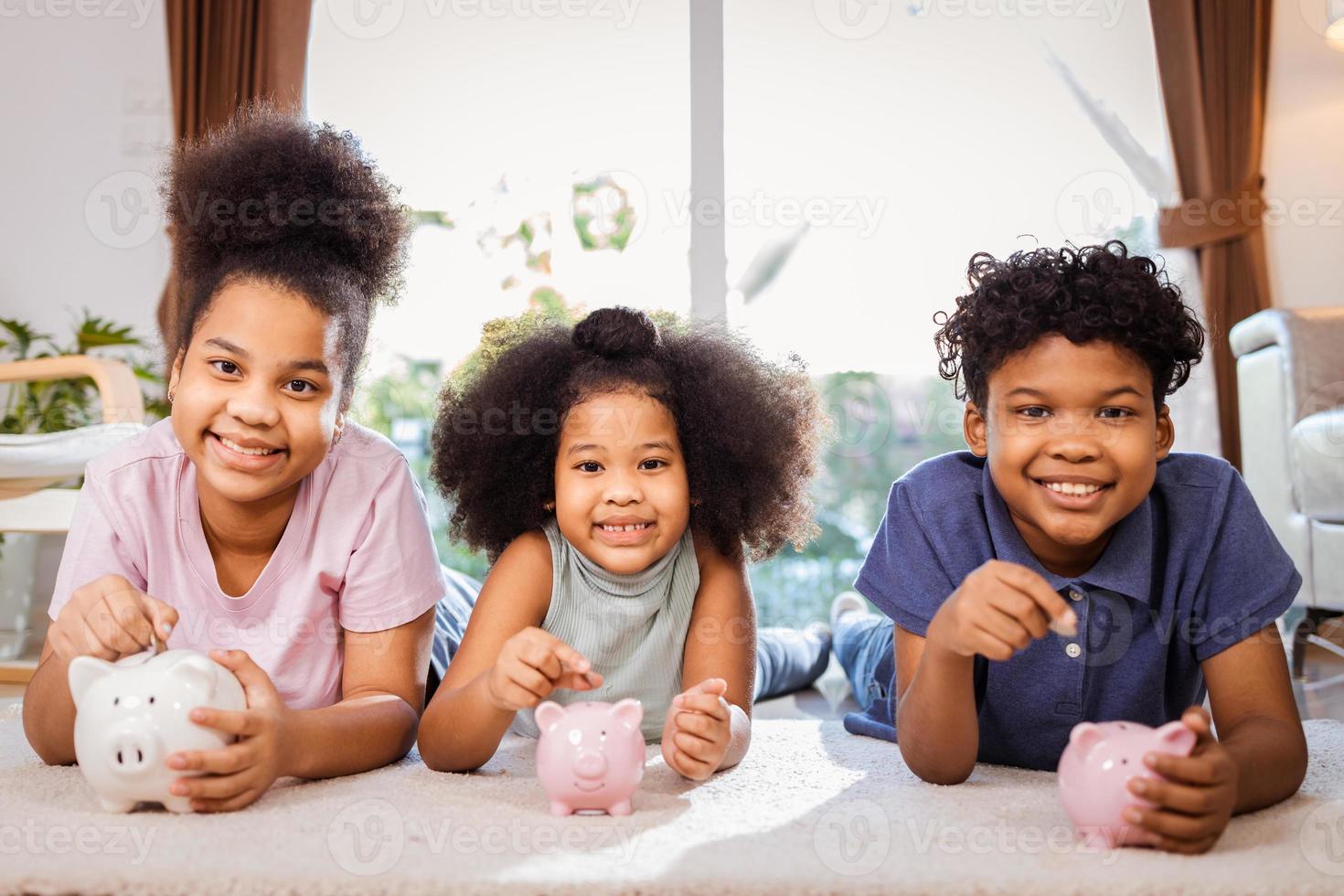 Porträt von afroamerikanischen Kindern, die zu Hause in einem Sparschwein im Wohnzimmer Geld sparen foto