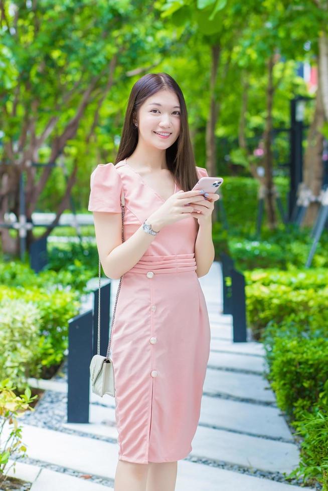 asiatische professionelle geschäftsfrau mit langen haaren lächelt im garten, während sie auf das tablet in ihrer hand schaut, arbeit von überall konzept. foto