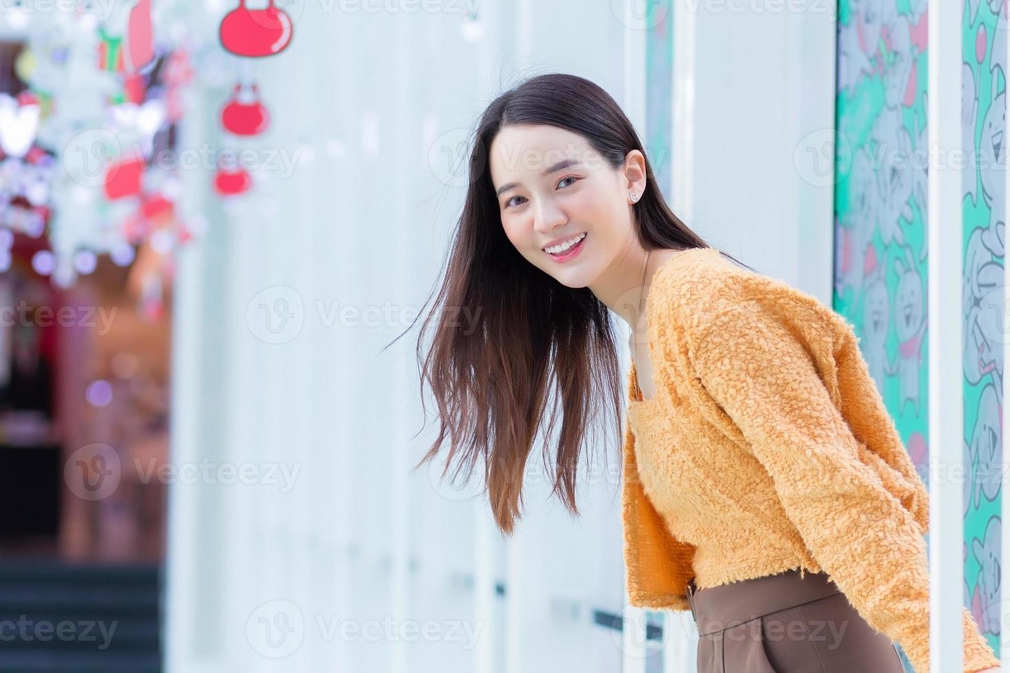 schöne asiatische frau mit langen haaren trägt gelben mantel und lächelt glücklich. im thema um weihnachten und ein frohes neues jahr zu feiern foto