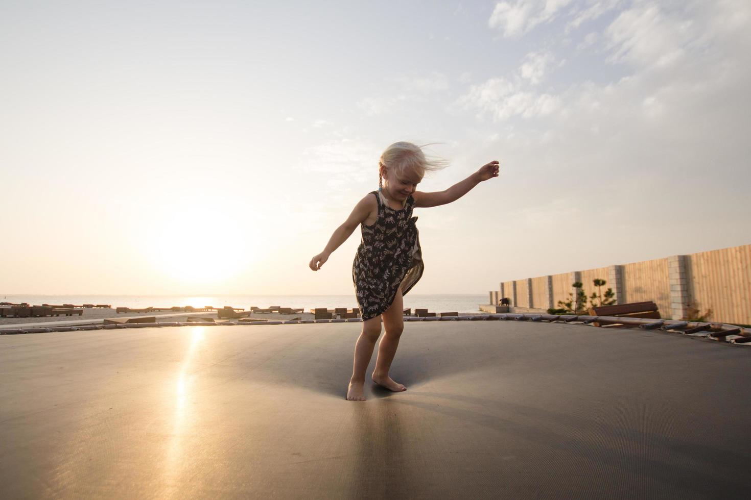 Kleines Mädchen springt und hat im Sommer eine gute Zeit auf dem Trampolin foto