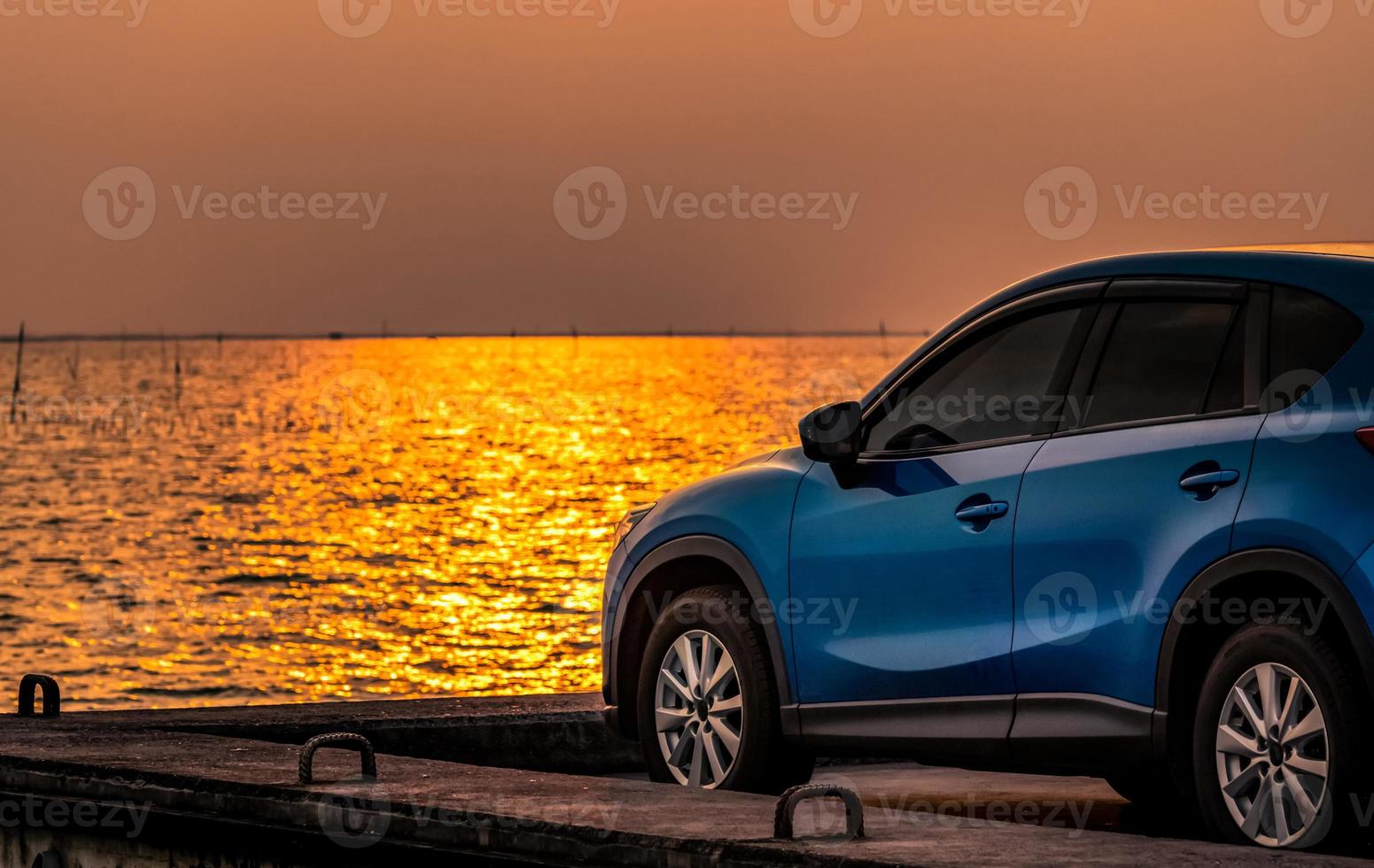 blaues kompaktes suv-auto mit sport und modernem design, das bei sonnenuntergang auf einer betonstraße am meer geparkt ist. umweltfreundliche Technologie. Elektroautotechnologie und -geschäft. Hybridauto und Automobil. foto