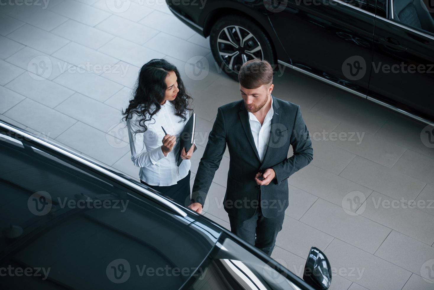 Denken Sie daran, was Sie bei der Besprechung sagen sollen. Kundin und moderner stylischer bärtiger Geschäftsmann im Autosalon foto