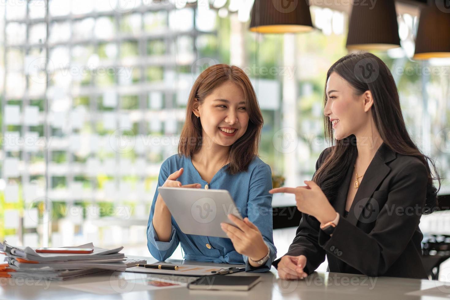 Zwei junge asiatische Geschäftsfrauen unterhalten sich in einer Gruppensitzung am Bürotisch in einem modernen Bürointerieur. Business Collaboration Strategische Planung und Brainstorming von Mitarbeitern foto