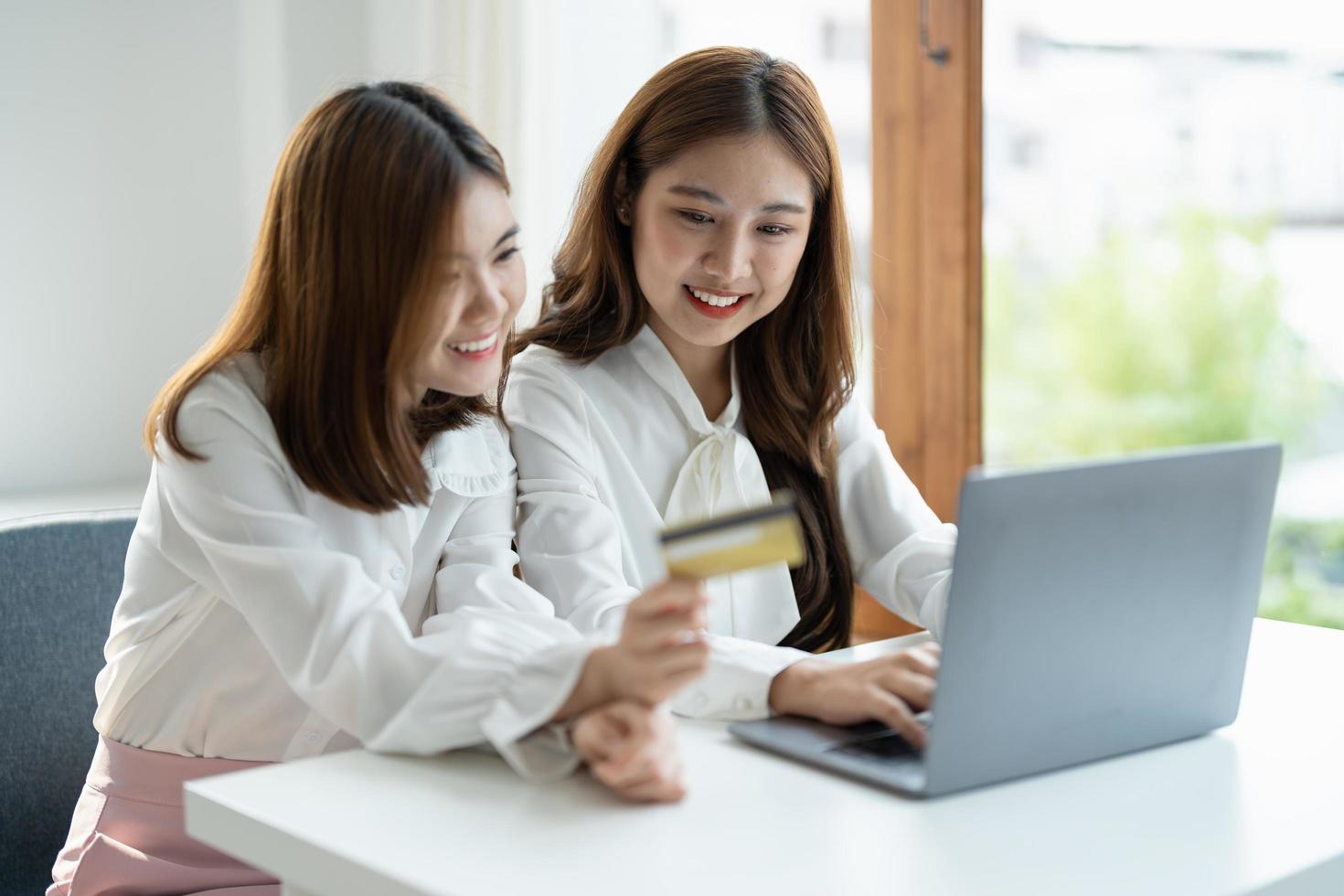 Zwei asiatische Freundinnen kaufen online mit Smartphone und Kreditkarte zu Hause ein. foto