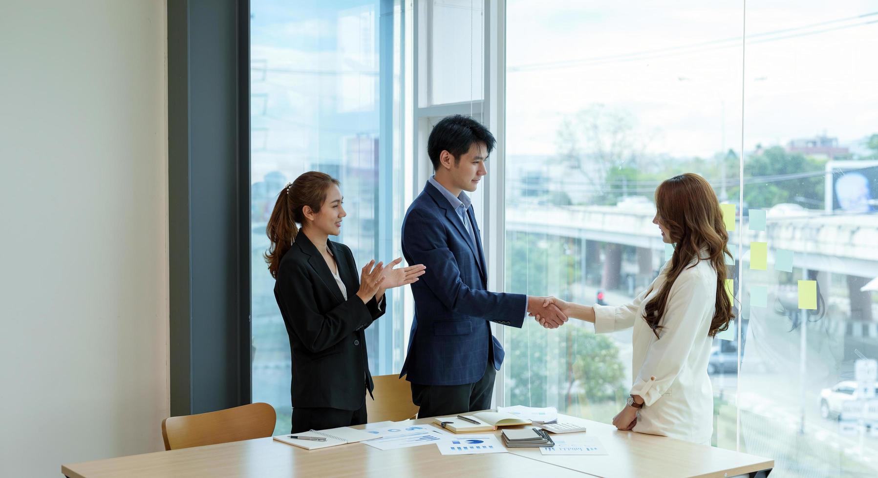 Geschäftsfrau applaudiert und gratuliert, während zwei Geschäftsleute ihre Hand schütteln, nachdem sie einen Deal oder eine Vereinbarung getroffen haben. Arbeits- und Erfolgskonzept. foto