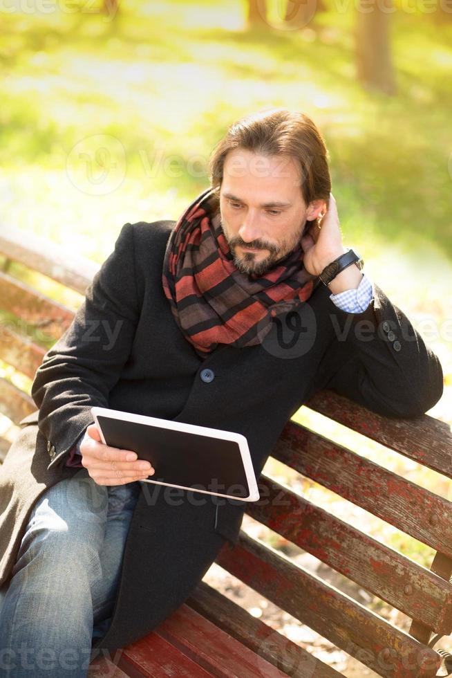 Mann mittleren Alters, der draußen auf der Bank ruht foto