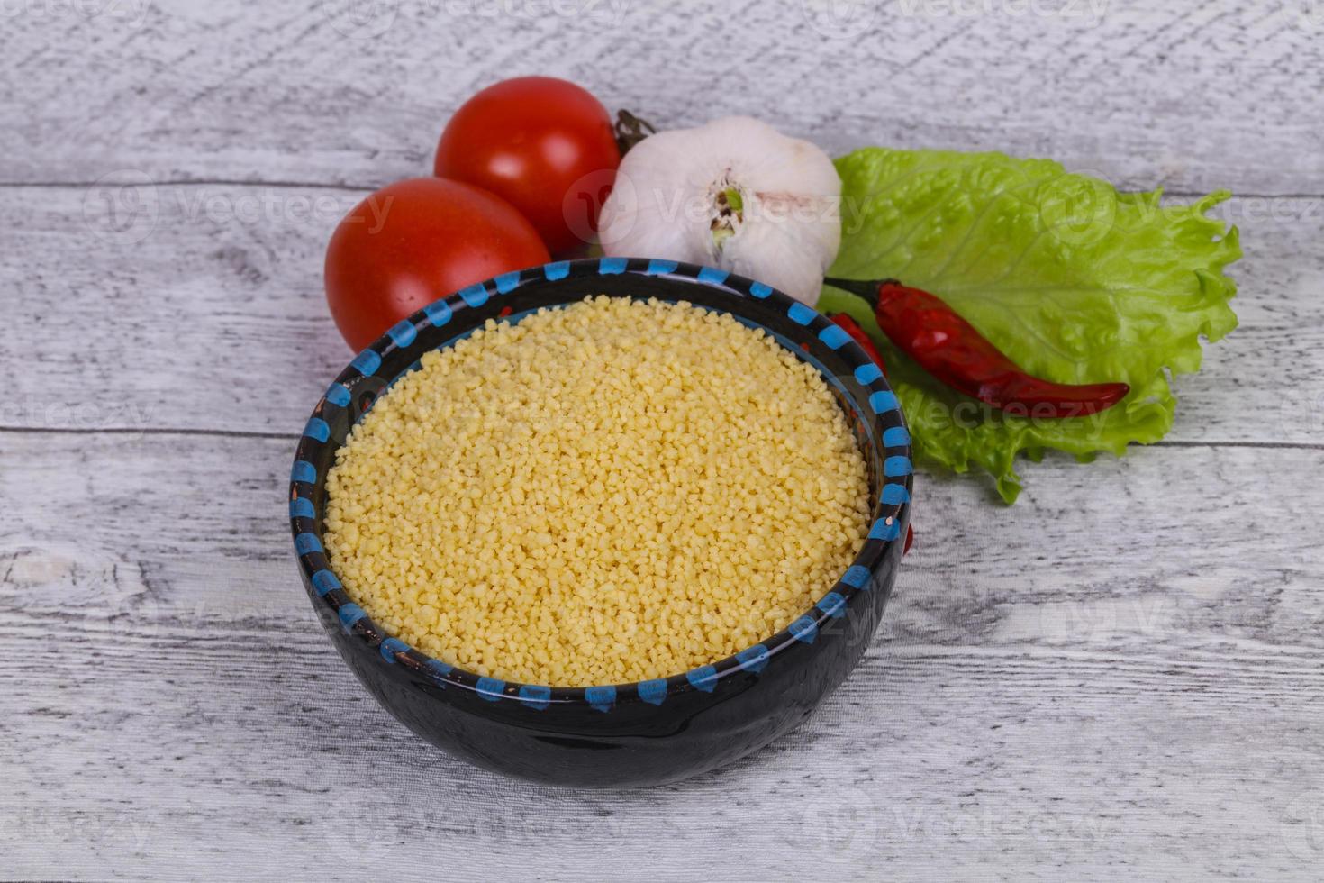 roher Couscous in der Schüssel serviert Salatblätter, Tomaten und Paprika foto