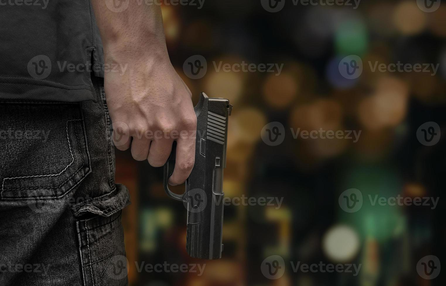 männliche hand, die pistole auf hintergrundnachtlicht-bokeh in der stadt hält foto