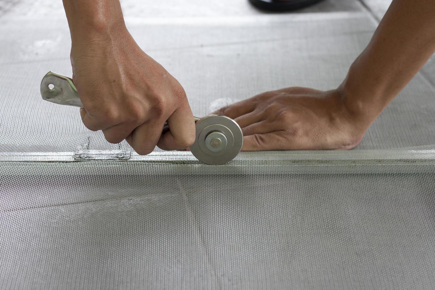 Hand eines Arbeiters, der ein Radwerkzeug hält, um ein Moskitonetz aus Aluminium zu installieren, das am Fenster des Hauses befestigt werden soll, um Insekten zu verhindern. foto