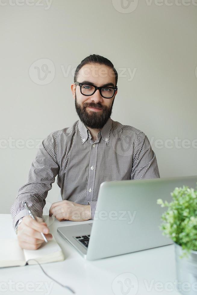 Mann mit Bart in Gläsern, die Notizen mit Laptop-Notizblock machen foto