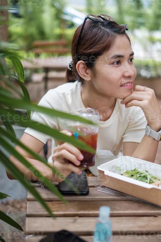 glückliche schöne frau, die im café lächelt und fröhlich ist, junges asiatisches mädchen, das eiskaffee hält foto