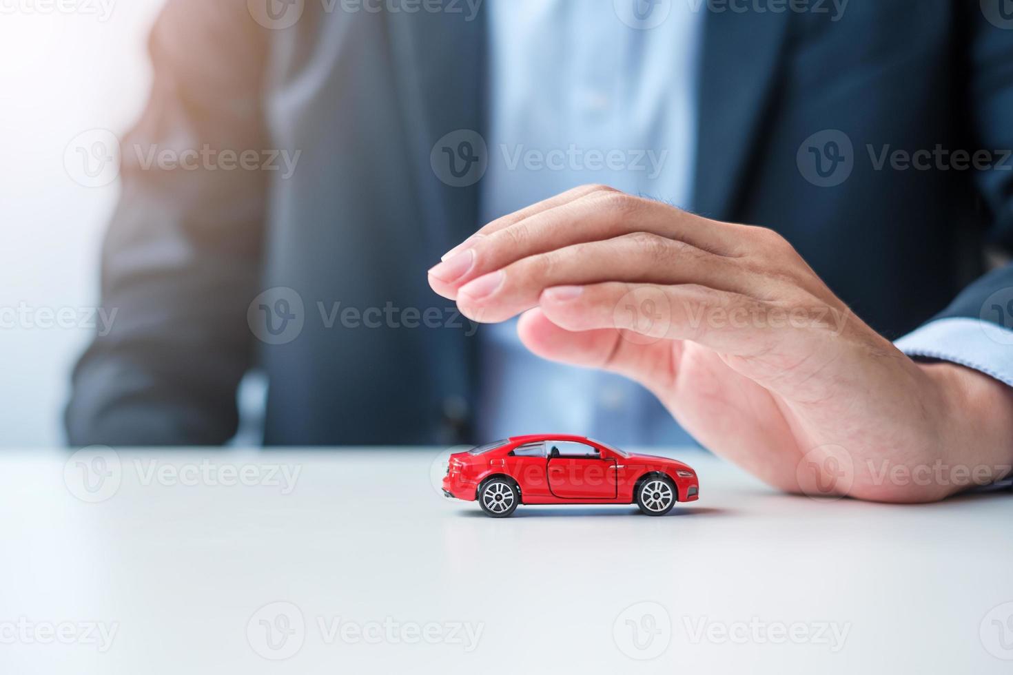 Geschäftsmann Handabdeckung oder Schutz rotes Autospielzeug auf dem Tisch. autoversicherung, garantie, reparatur, finanz-, bank- und geldkonzept foto