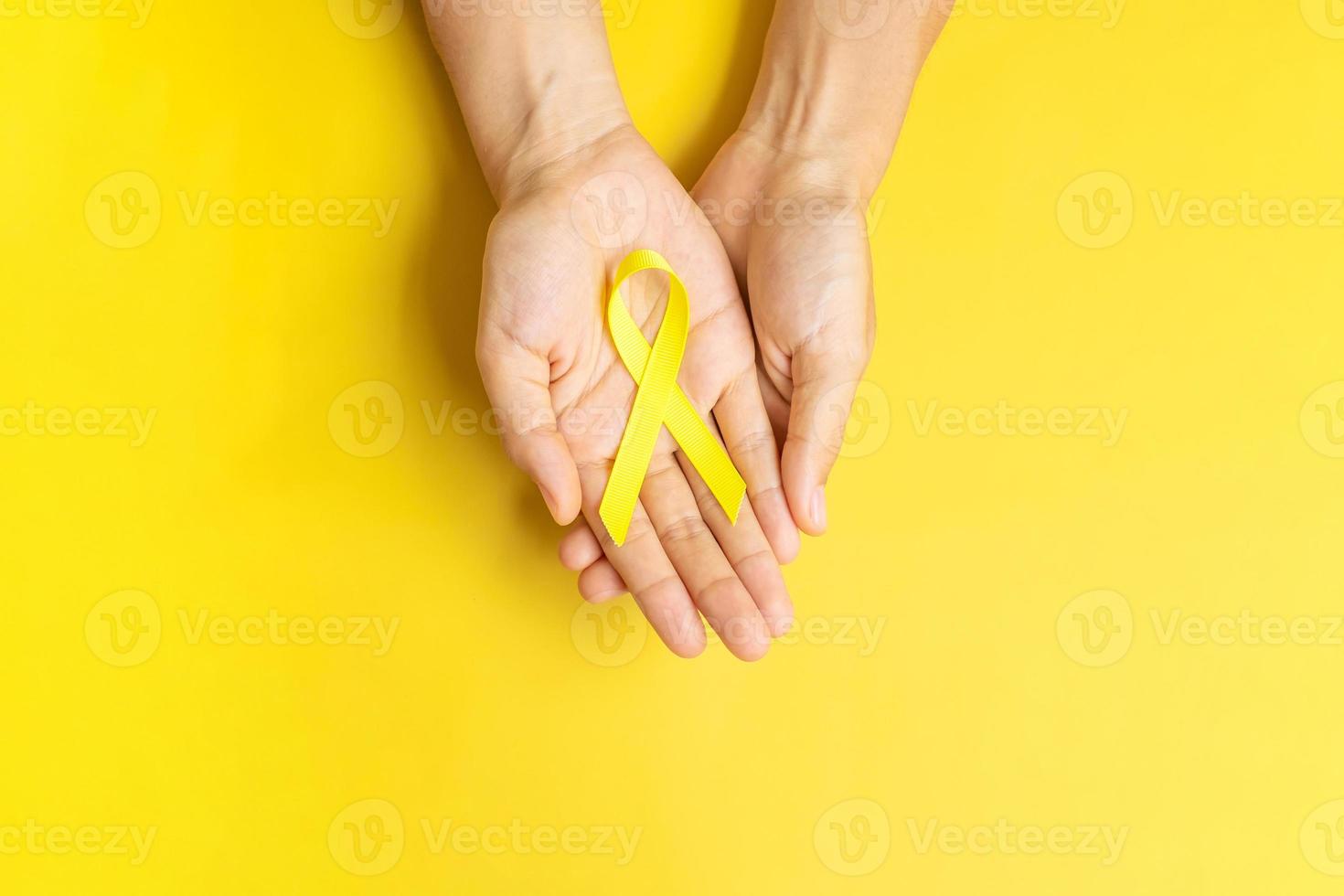 Hand, die ein gelbes Band auf gelbem Hintergrund hält, um Menschen zu unterstützen, die leben und krank sind. Tag der Suizidprävention im September, Monat des Bewusstseins für Krebs im Kindesalter und Konzept des Weltkrebstages foto