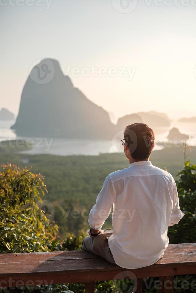 glücklicher reisender mann genießen sie den aussichtspunkt der phang nga bucht, alleintourist sitzen und entspannen in samet nang sie, in der nähe von phuket in südthailand. reise-, reise- und sommerferienkonzept in südostasien foto